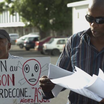 Sur cette photo du 18 novembre 2007, l'avocat Harry Durimel, à droite, se tient à côté d'un militant avec une pancarte indiquant "Non au poison du chlordécone", alors qu'ils protestent lors de l'arrivée de la ministre française de la Santé, Roselyne Bachelot à Raizet Abymes. Durimel fait alors partie des avocats représentant les travailleurs agricoles de Guadeloupe et de Martinique qui luttent depuis longtemps pour obtenir une compensation pour l'utilisation d'un pesticide interdit, le chlordécone. Photo Sipa / AP / Dominique Chomereau-Lamotte Sur cette photo du 18 novembre 2007, l'avocat Harry Durimel, à droite, se tient à côté d'un militant avec une pancarte indiquant "Non au poison du chlordécone", alors qu'ils protestent lors de l'arrivée de la ministre française de la Santé, Roselyne Bachelot à Raizet Abymes. Durimel fait alors partie des avocats représentant les travailleurs agricoles de Guadeloupe et de Martinique qui luttent depuis longtemps pour obtenir une compensation pour l'utilisation d'un pesticide interdit, le chlordécone. Photo Sipa / AP / Dominique Chomereau-Lamotte